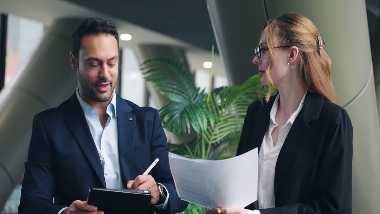 Zwei professionelle KollegInnen besprechen ernsthaft ein Projekt und überprüfen Dokumente, feiern dann ihre erfolgreiche Teamarbeit und ihre Leistung mit einem freudigen High-Five in einem modernen Büro