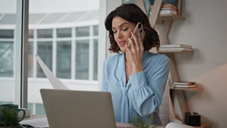 Successful entrepreneur calling smartphone looking laptop at office desk closeup