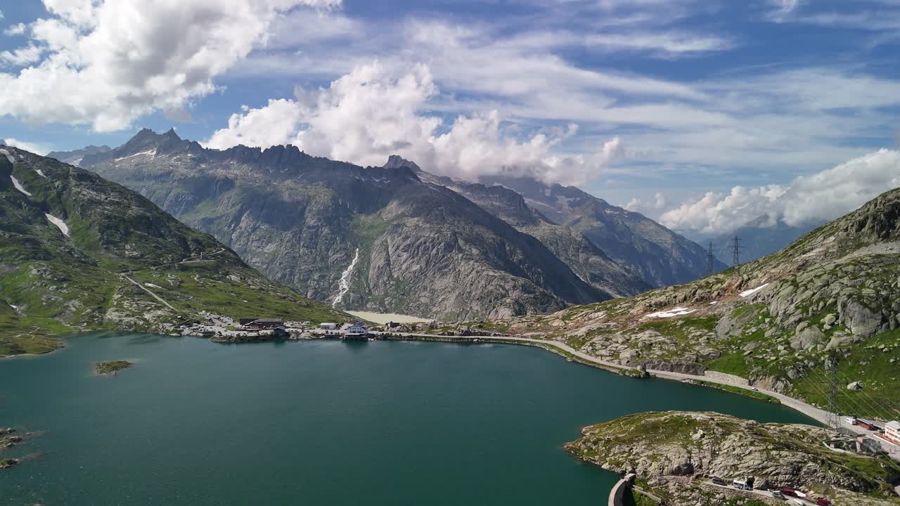 Aerial view of Lake Totensee set amidst the mountain range in Obergoms, Switzerland, highlighting the striking contrast between the tranquil lake and the rugged alpine landscape.