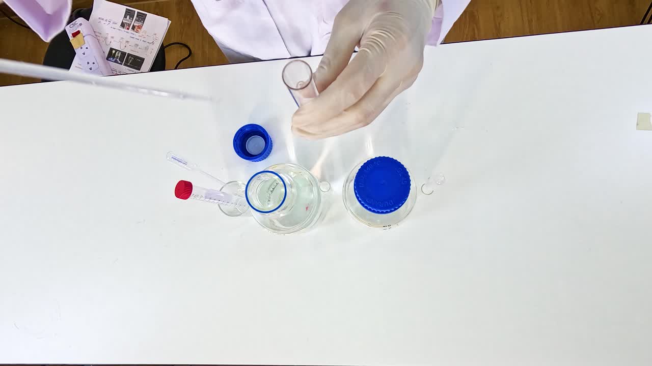 Hands in gloves conduct a chemical experiment with glassware on a white table under bright lighting