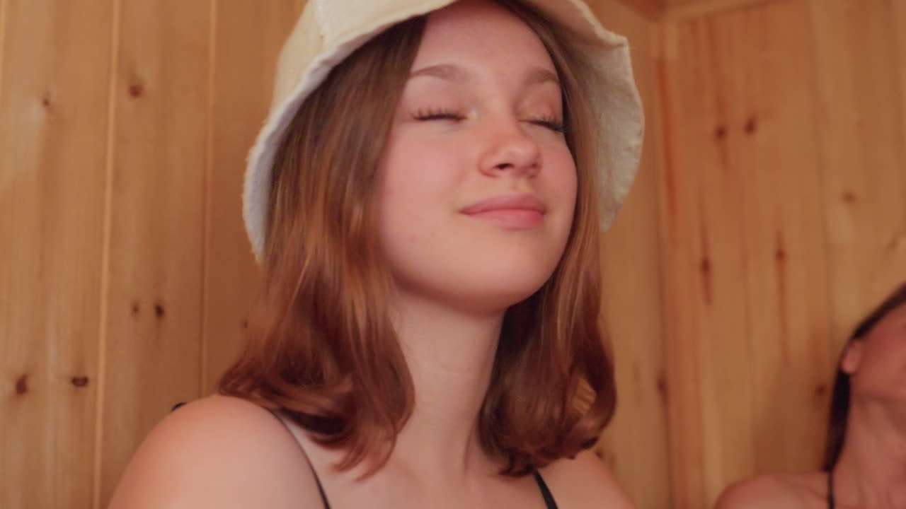 Woman relaxing on grey towel, eyes closed and smiling, enjoying peaceful moment in cozy wooden sauna, the serene atmosphere and warm wooden surroundings