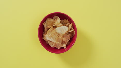 close up of potato chips in a bowl with copy space on yellow surface