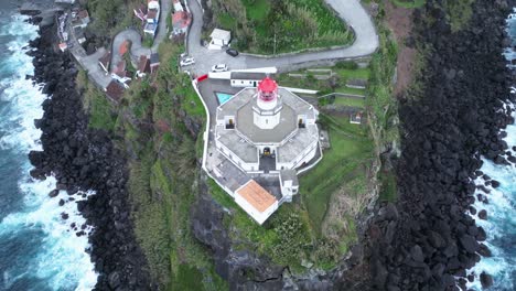 Lighthouse-at-Portuguese-sea-green-cliff,-aerial-drone-reveals-Azores-Landmark