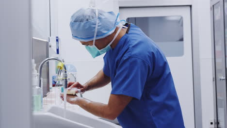 male surgeon wearing scrubs washing hands before operation in hospital operating theater