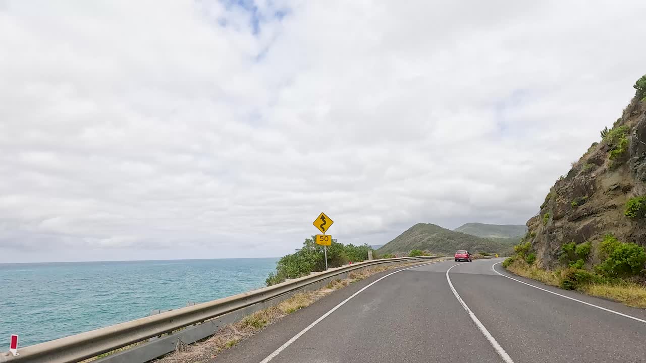 A 13-second video captures a drive along the Great Ocean Road, showcasing coastal views, winding roads, and lush greenery under cloudy skies