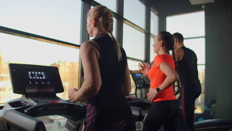 a group of people running on a treadmill in a fitness room performing a cardio workout. men and women train together running indoors warm-up before training in slow motion.