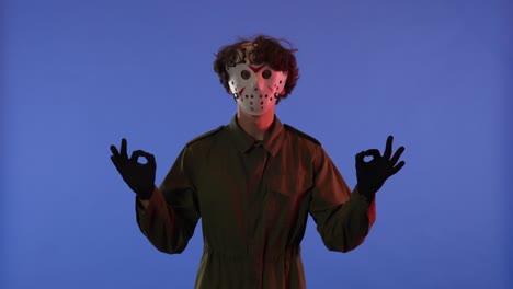 man in white mask looking around and showing like gesture with fingers on blue background with red