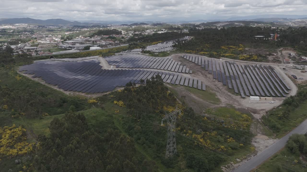 aerial shot of large solar panel installation on hills near town and forested landscape