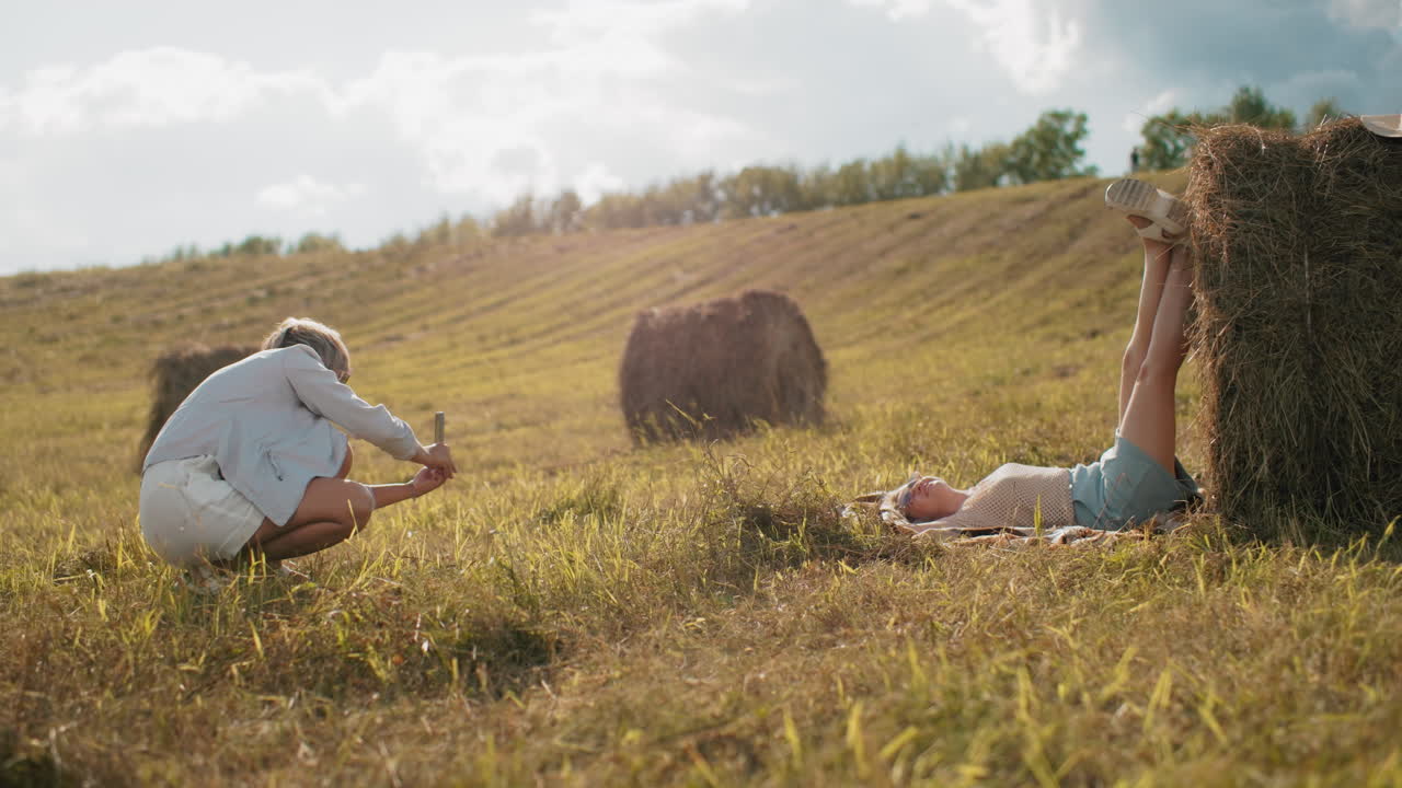 사진작가는 그녀의 여동생을 야외에서 포착합니다. 그녀는 넓은 농지에서 풀에 다리를 놓습니다. 은 날, 편안한 시골 분위기, 자연의 창의성.