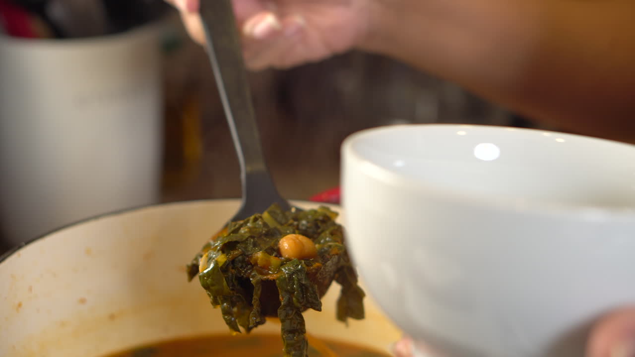 Scooping a ladle of kale and chickpea soup into a serving bowl - close up
