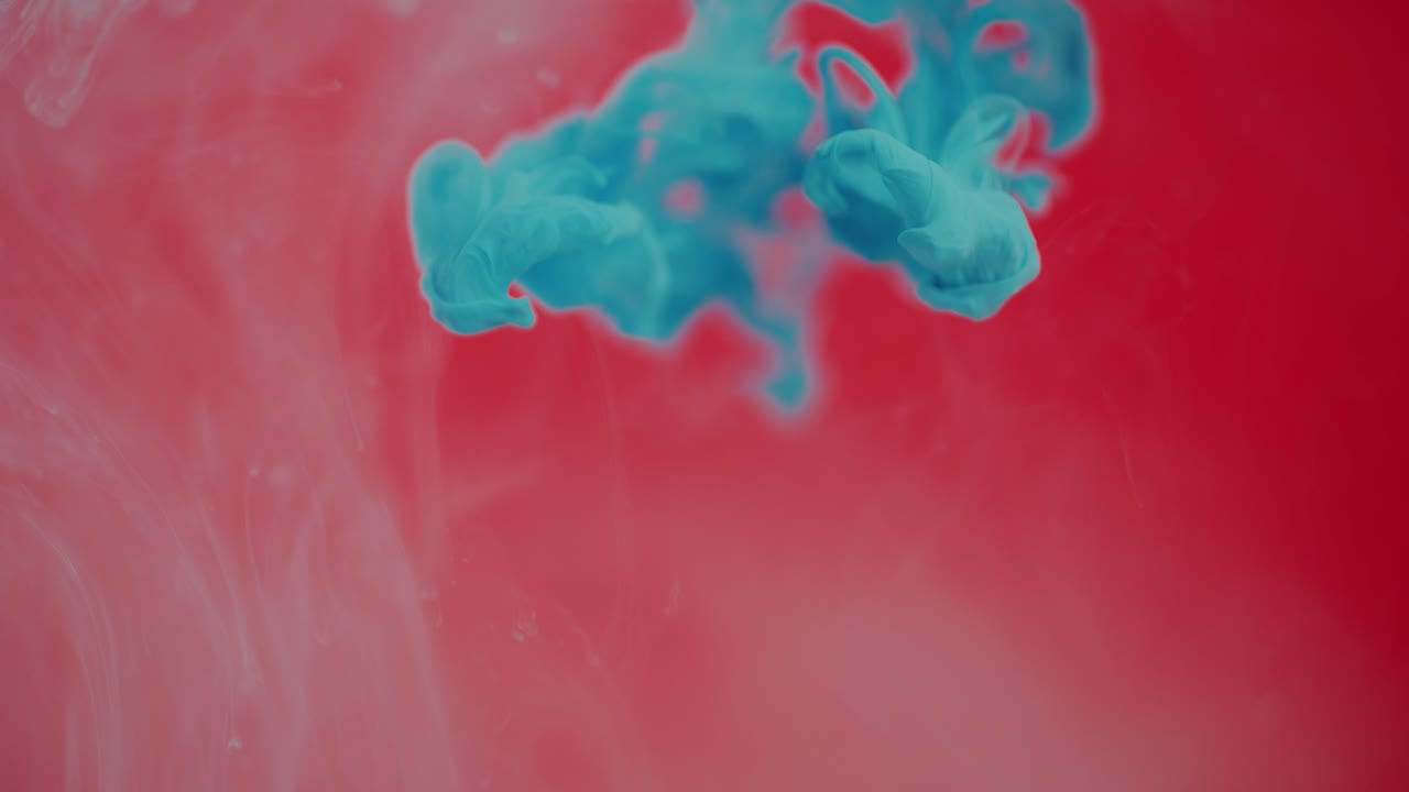 gotas de tinta azul y pintura cayendo en un tanque de agua sobre un fondo rojo
