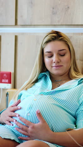 woman on the last stages of pregnancy lies on bed in hospital. future mom stroking her big belly while receiving medicine from drop counter. vertical video
