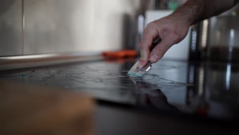 man cleaning the ceramic glass of his kitchen with special product and a scraper