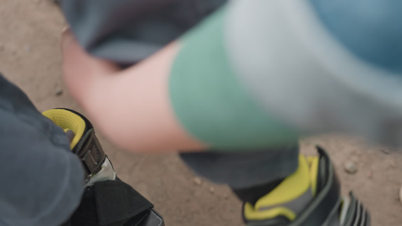 CloseUp Hand Securing Shoe Strap On Wheelchair Footrest, Careful Buckle Action And Protective Support, Athletic Sneaker And Ankle Visible, Outdoor Ground And Calming Caregiving Scene Emphasizing