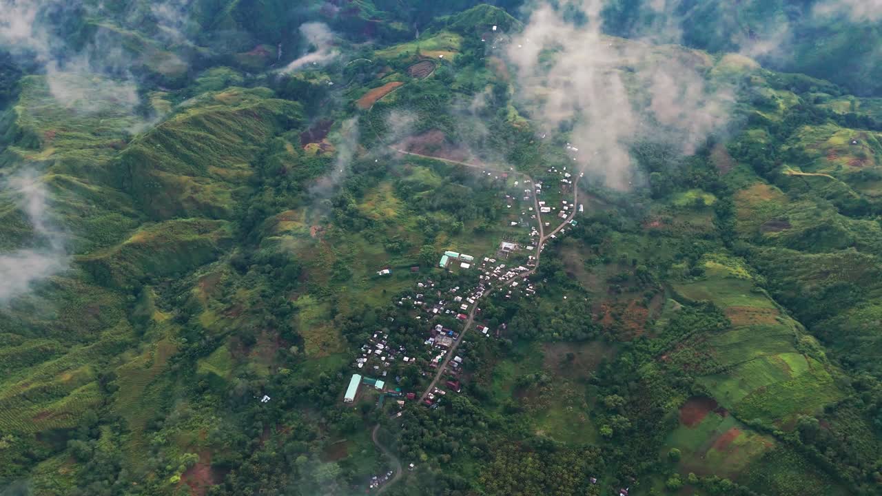 aerial view of a rural village in the mountains of the Philippines, surrounded by lush greenery and mist. Captured in the morning, showcasing the peaceful atmosphere and natural beauty