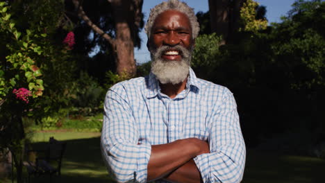 portrait of smiling african american senior man standing in sunny garden