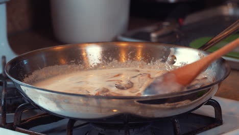 stirring sliced mushrooms simmering in a brown sauce in a skillet on the stove