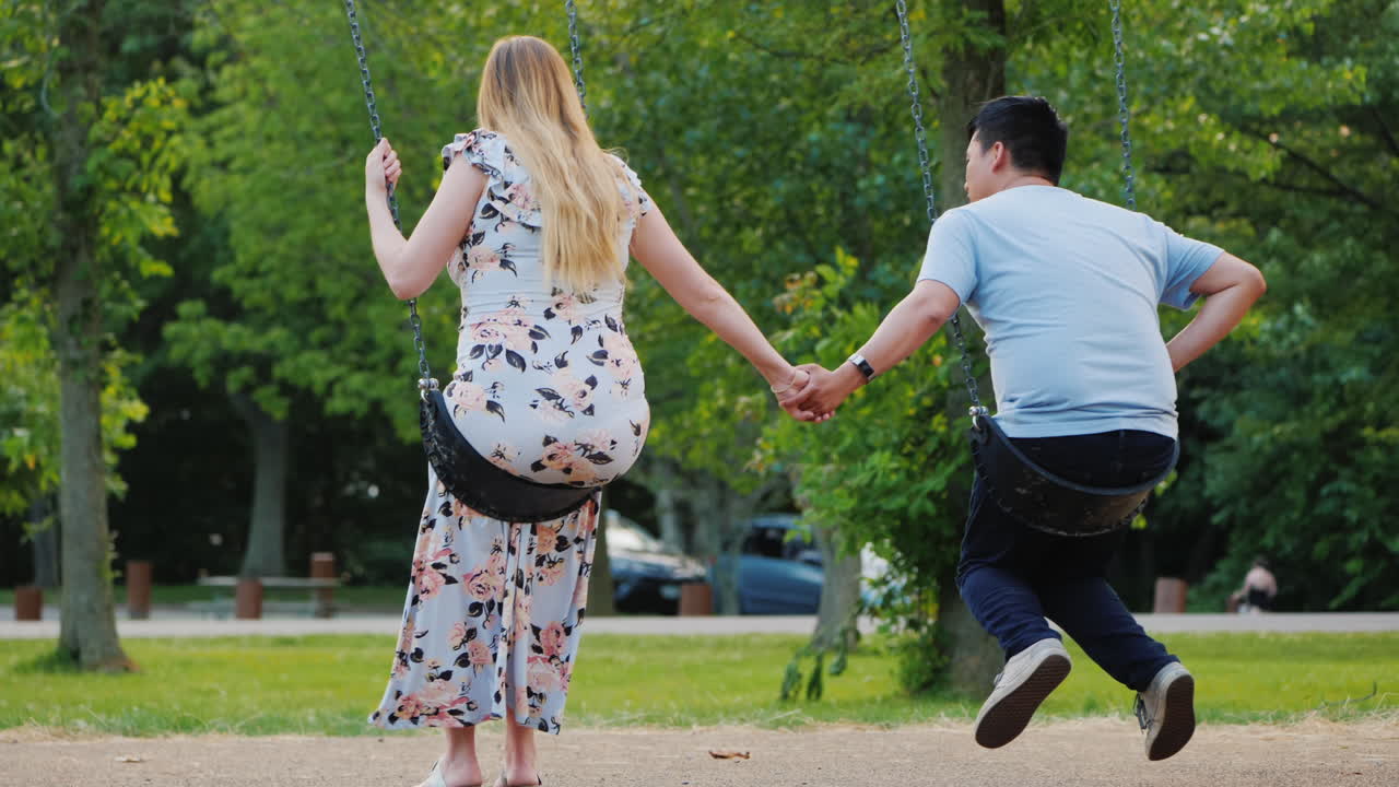 다민족 커플 - 아시아 남자와 임신한 백인 여자가 그네를 타고 행복한 젊은 가족