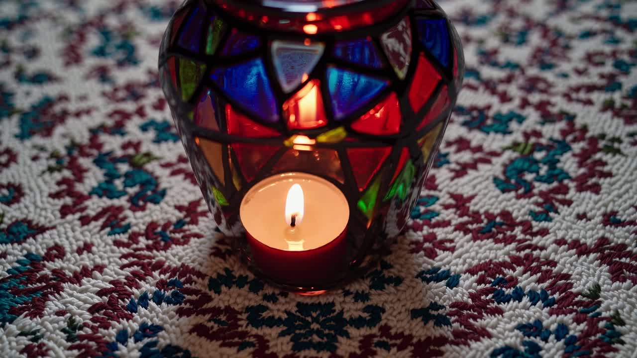 Vibrant stained glass candle holder with a lit tea light inside sits on a decorative crocheted doily, creating a warm and inviting atmosphere