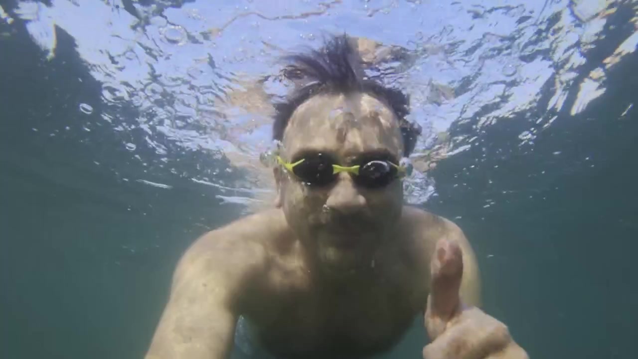 Uomo con occhialini da nuoto che si immerge sott'acqua con il cielo azzurro limpido che si riflette sulla superficie dell'acqua, godendosi le vacanze estive