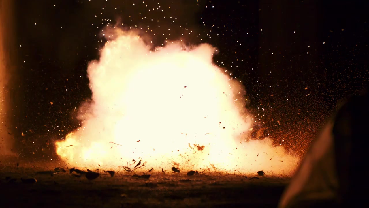 Scintille e braci ardenti esplodono e si disperdono nell'ambiente notturno buio all'aperto con effetti di fumo e fiamme.