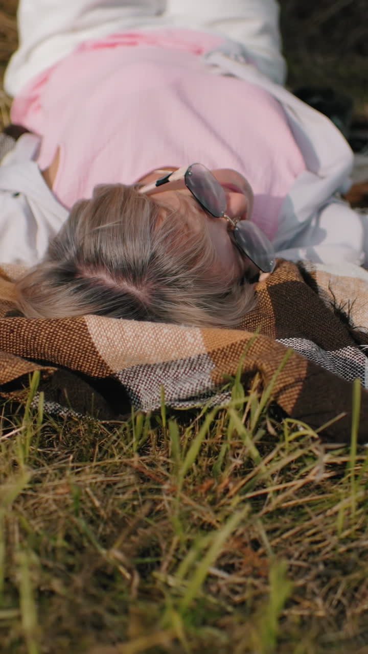 한 여성이 스마트워치로 친구의 사진을 찍고 에 누워서 다리를 공중으로 들어 올려 시골의 야외에서 빛이 고 자연에서 재미있고 편안한 순간을 포착합니다.