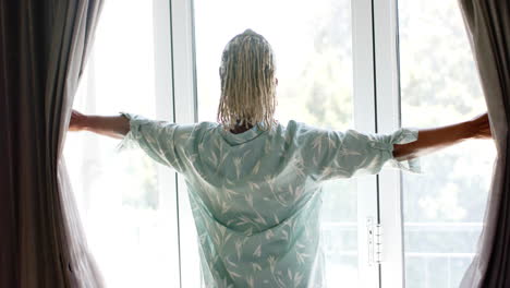 a senior african american woman is opening curtains to let light in