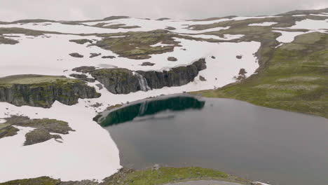 vista desde la carretera de montaña de la impresionante cascada en un acantilado rocoso cubierto de nieve en aurland, noruega