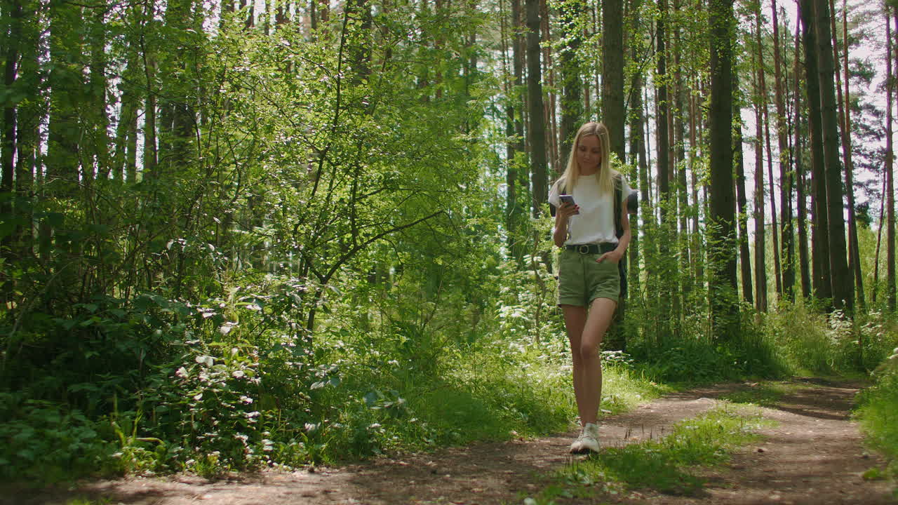 mujer atractiva relajándose en el bosque y usando un teléfono inteligente al aire libre. mujer caminando en el bosque y escribiendo mensajes en el teléfono inteligente. mujer excursionista en solitario usando un teléfono inteligente.