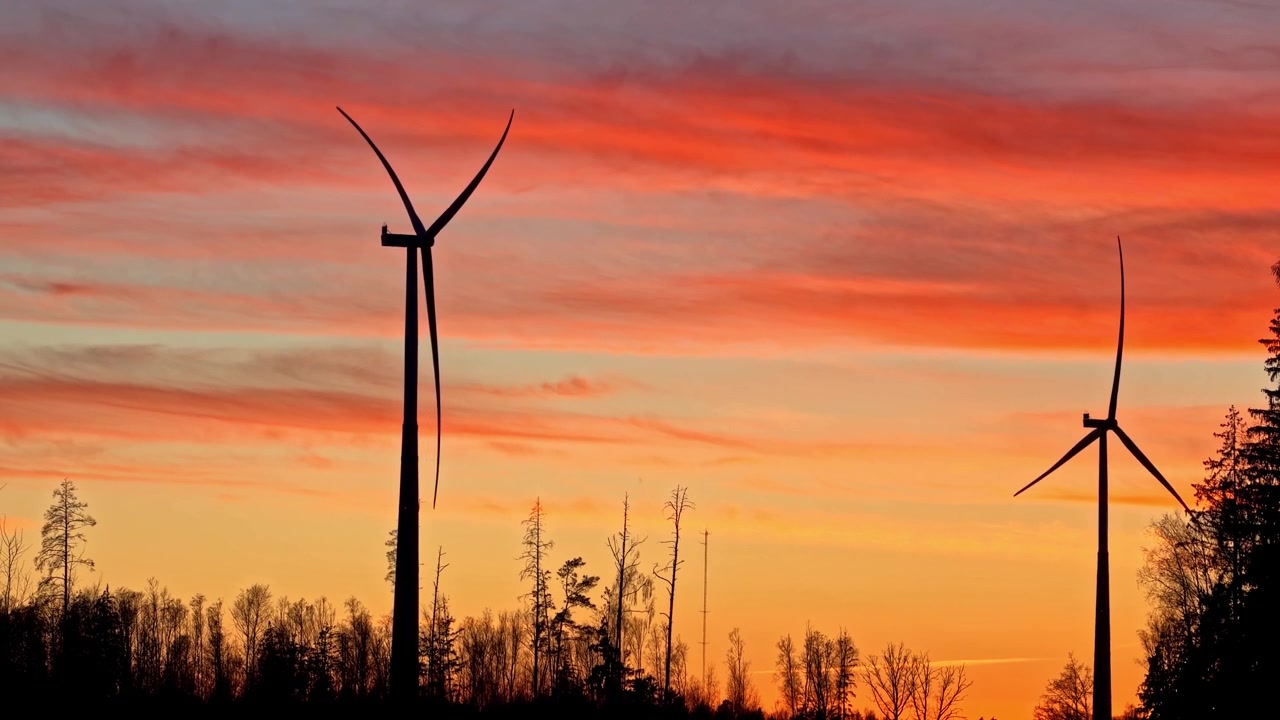 Vindturbiner som produserer ren energi med roterende blader under en fargerik og dramatisk solnedgang