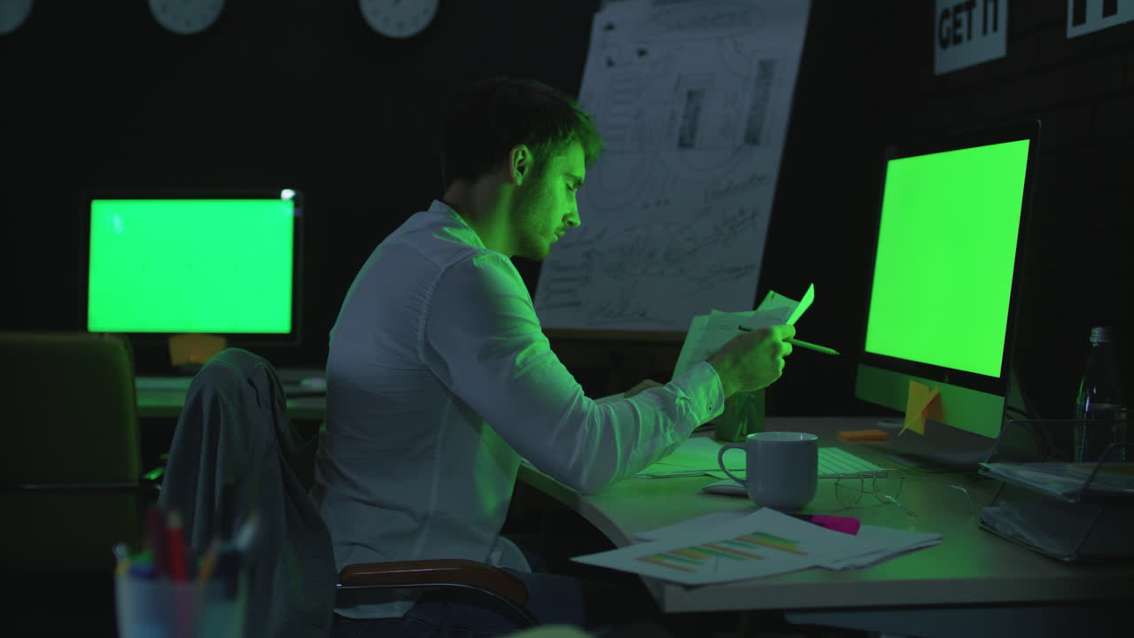 Young businessman working on computer with green monitor in night office.