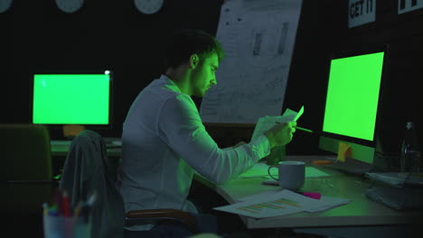 Young-businessman-working-on-computer-with-green-monitor-in-night-office.