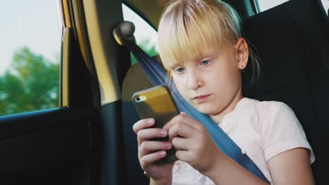 technology on the road. the girl  playing on a smartphone, she is riding a car seat