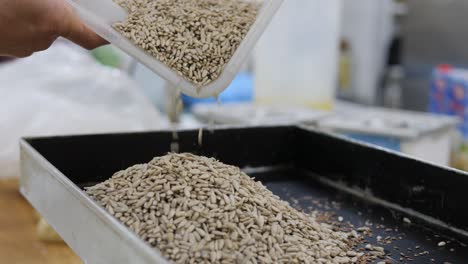 pastry chef pours pine seeds into baking tray to prepare cereal bars