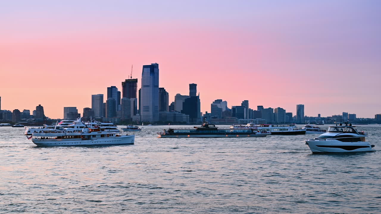 Multiple diverse cruise boats stand on the waterscape at sunset. Skyline of New York at the backdrop of pink sky