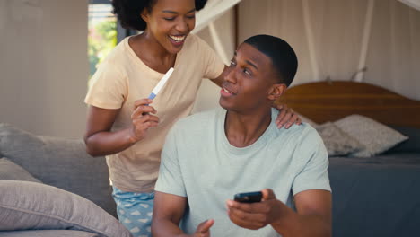 Excited-Couple-In-Bedroom-At-Home-Celebrating-Positive-Pregnancy-Test-Result