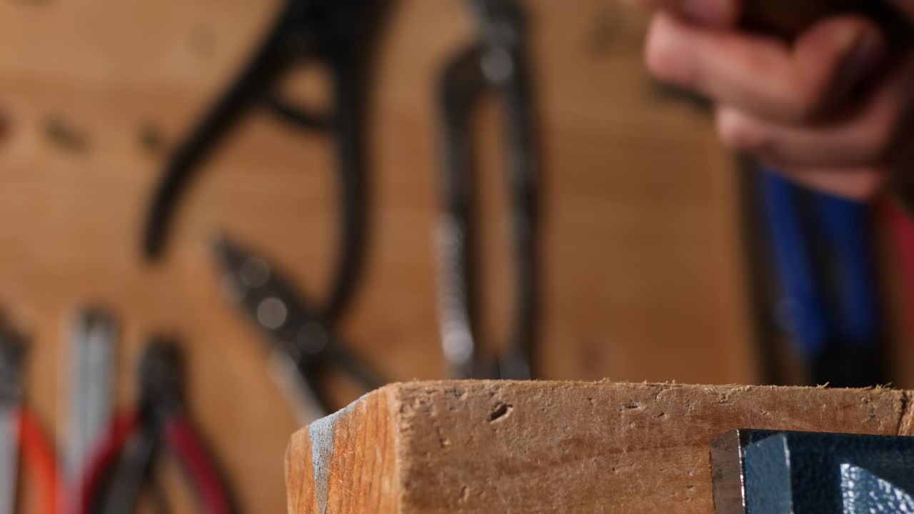 mano caucásica martillando un clavo en un trozo de madera en un taller casero de bricolaje