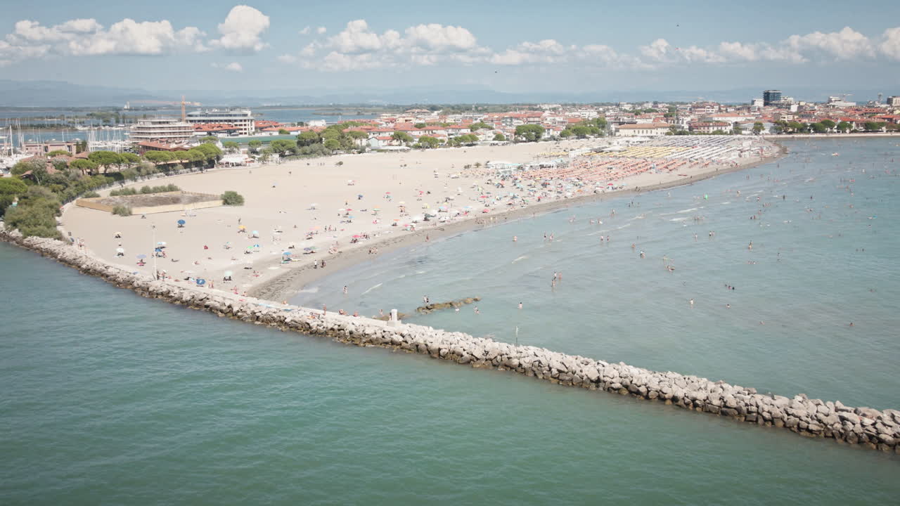 Drone 4K UHD si allontana fluidamente dalla spiaggia sabbiosa di Grado, rivelando un molo in pietra e il vasto Mare Adriatico—ideale per film di viaggio e inquadrature di apertura.