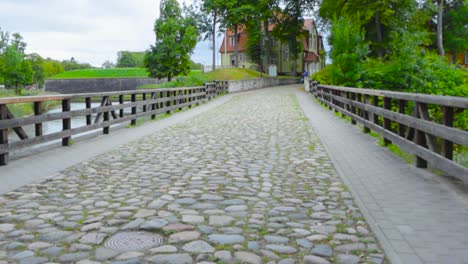 footage of a cobblestone road during summer day time with moss and grass growing between the rocks. in kuressaare estonia the bridge has wooder railings. bridge goes over a moat or a river.