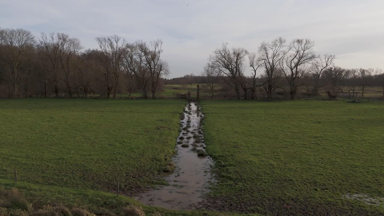 Drone shot of a brook gliding through grass lands after heavy rain during winter