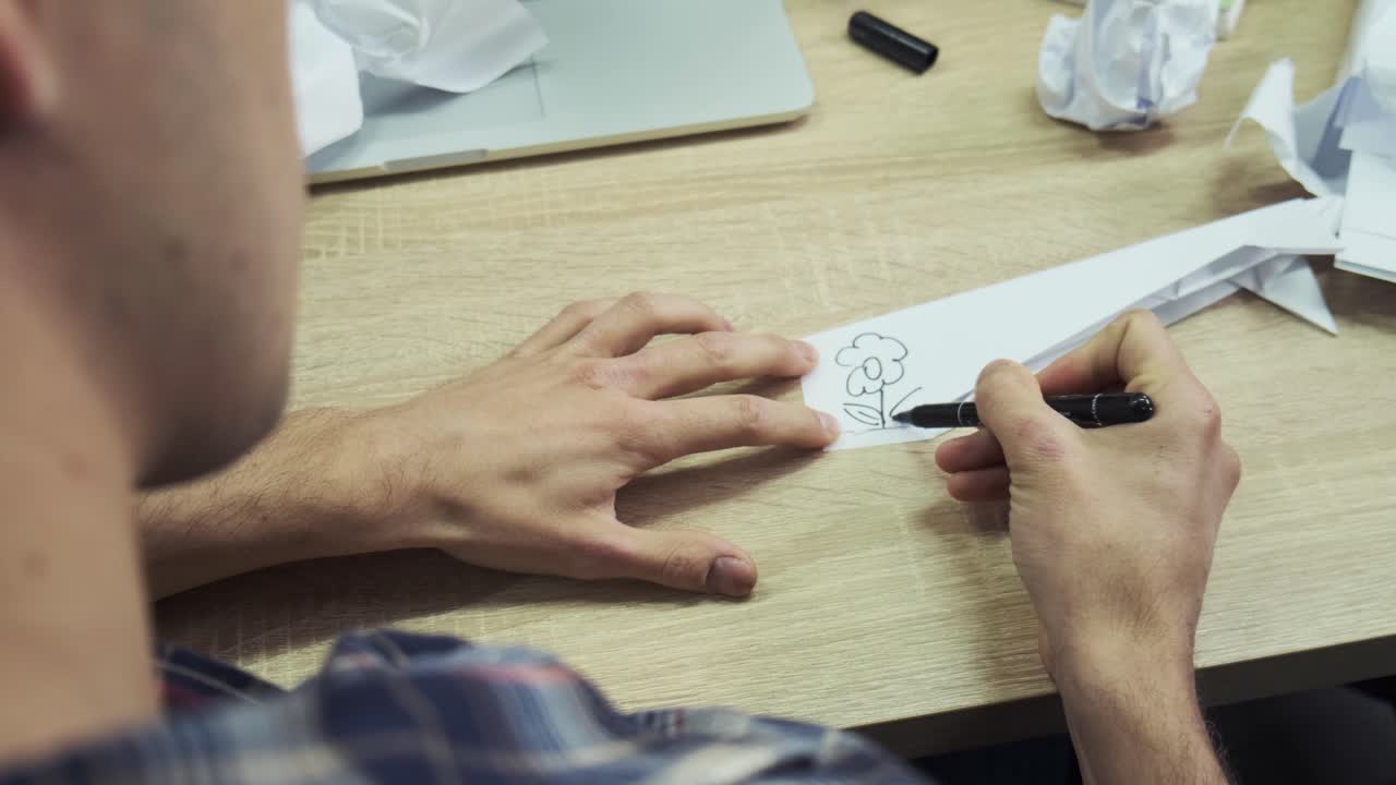 человек, рисующий цветок на бумаге за столом