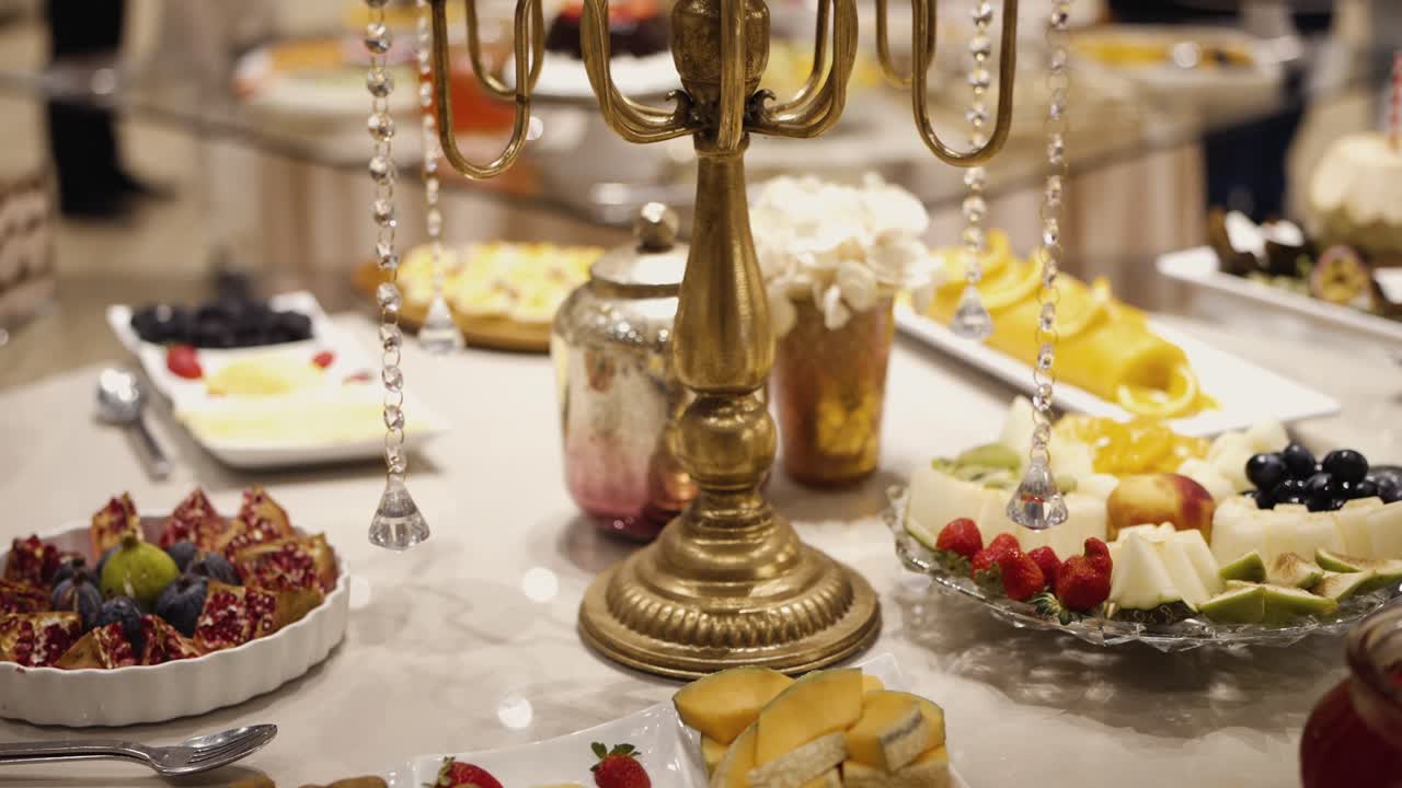 Buffet table with plates of fruit cheese desserts and sweets arranged around decorative candle holder