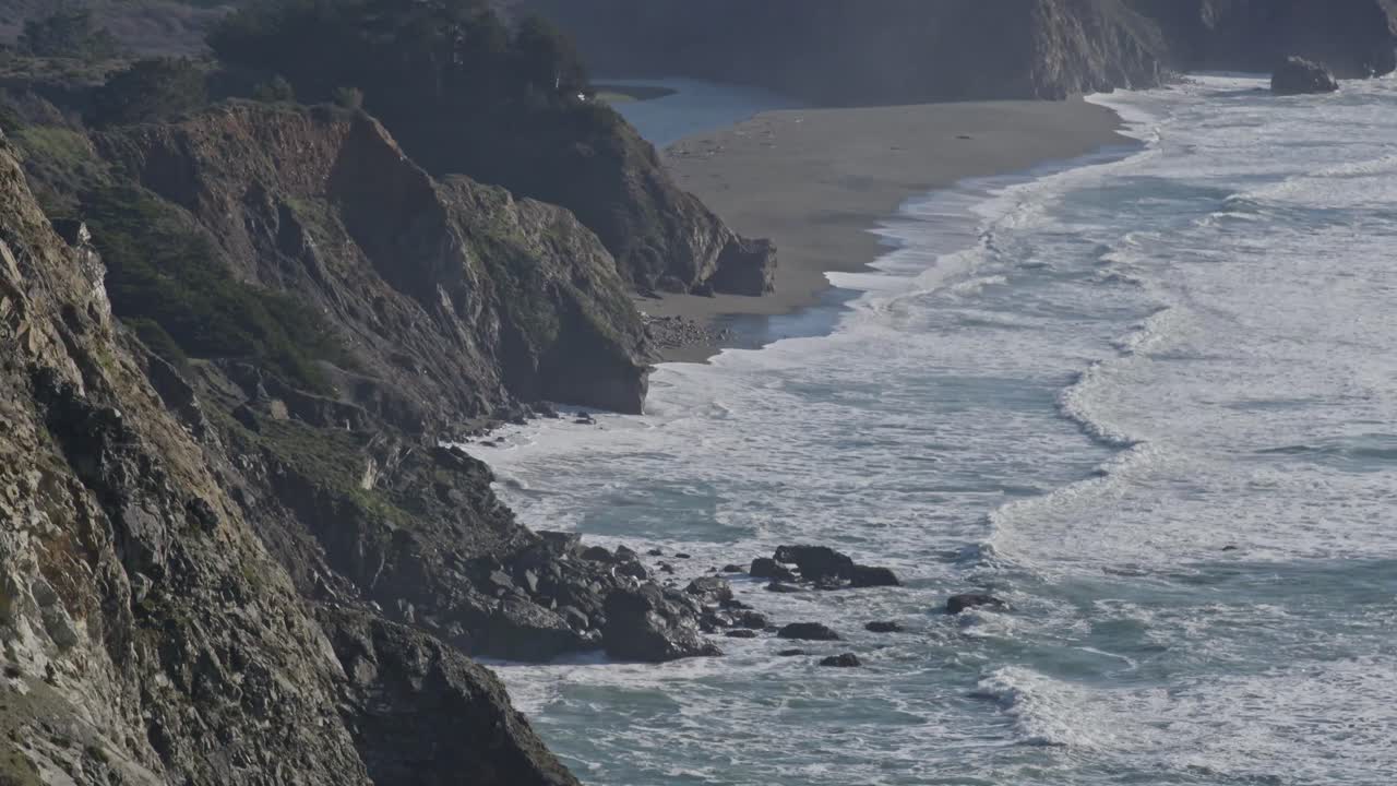 Cinematic drone shot glides past Big Sur’s iconic cliffs and rocky shoreline as waves crash against the base, revealing California's raw coastal beauty.