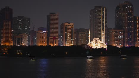 Nachtansicht-Der-Ikonischen-Al-Noor-Moschee-Von-Sharjah,-Des-Khalid-Sees-Und-Der-Al-Noor-Insel-Skyline-Der-Stadt-Sharjah-Im-Hintergrund,-Touristenboote-Im-Meer,-Vereinigte-Arabische-Emirate,-4K-Video