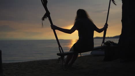 silueta de una mujer joven en un columpio al atardecer en una hermosa playa