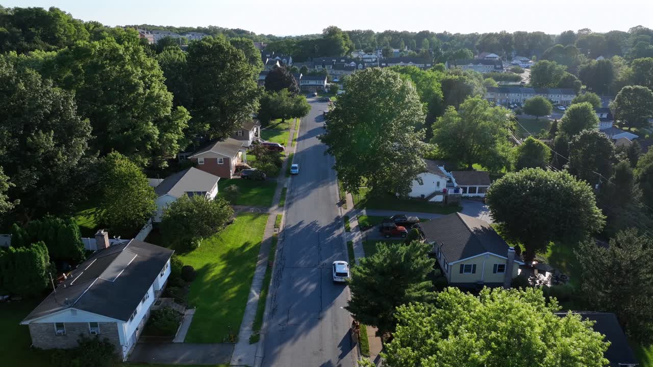 Single family houses in America suburb during sunny sunrise in summer. Cars on street. Aerial backwards top down. Green trees in idyllic district of town. Wide shot