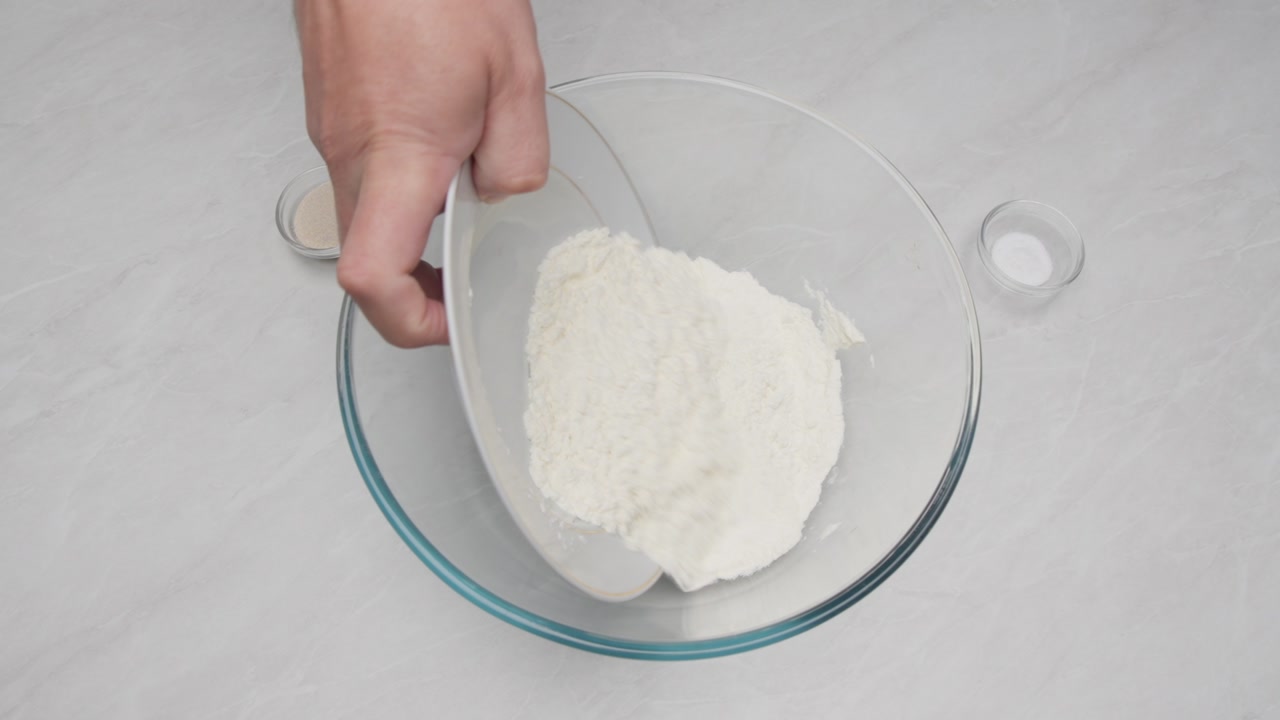Top down view of salt and yeast added to flour in a glass bowl