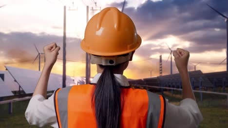 close up back view of a female engineer with safety helmet raising her hands celebrating while working with solar panel and wind turbines