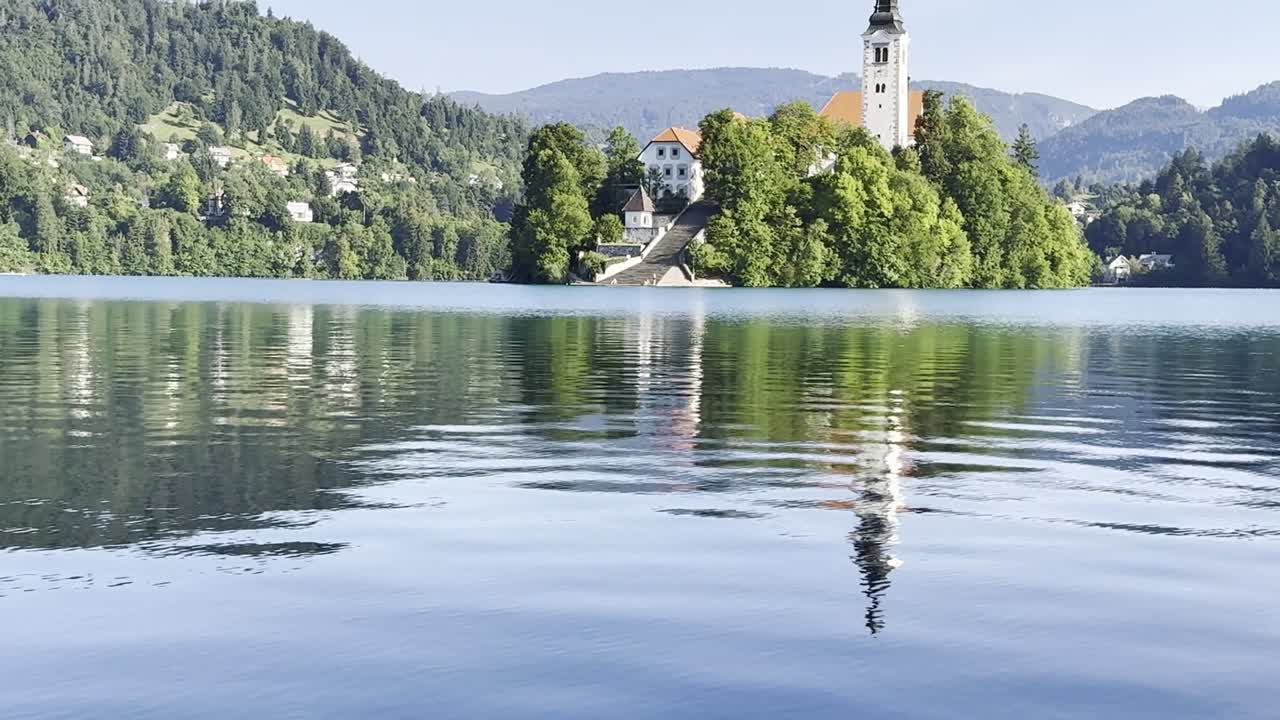 View onto Lake Bled Island and Church of the Assumption of the Blessed Virgin Mary with colourful reflections on a sunny summer morning