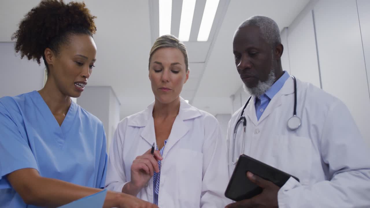 Médicos e profissionais de saúde de diversas etnias de pé no corredor do hospital e conversando.